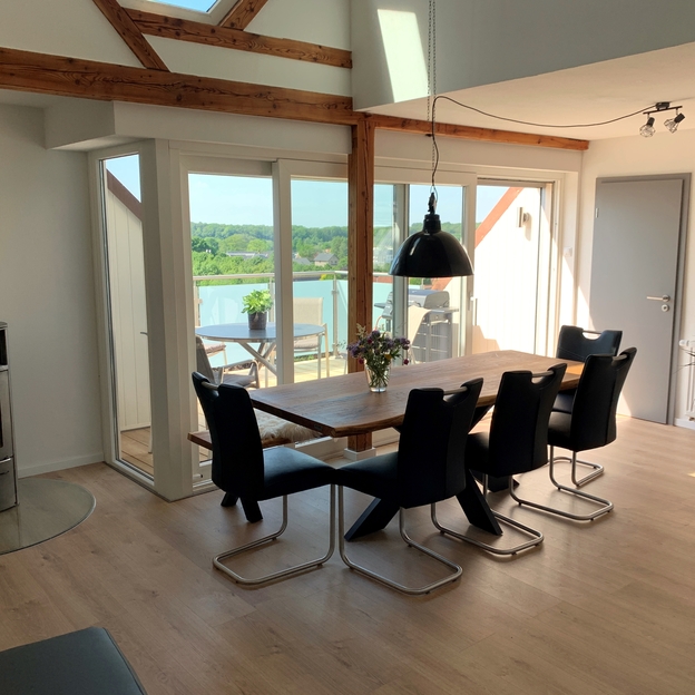 Holztisch vor Fensterfront und Kamin mit dunklen Stühlen