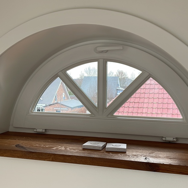 Einzigartiges Fenster nach Maß in Dreiecksform mit weißem Rahmen und einer dunklen Holzfensterbank, mit Blick auf Dachziegel.