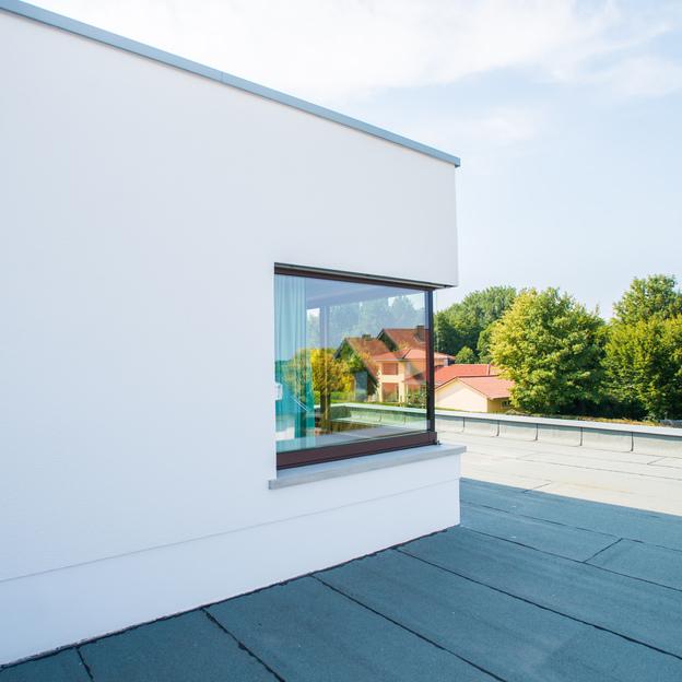 Ein modernes Haus mit einem stilvollen Eckfenster nach Maß, das eine klare Sicht auf die umliegenden Bäume und Dächer bietet.