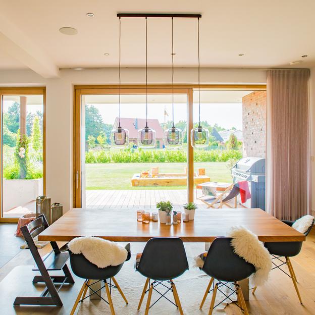 Geräumiges Esszimmer mit Holztisch, modernen Stühlen und großen Terrassentüren aus Fenstern nach Maß, mit Blick auf den Garten.