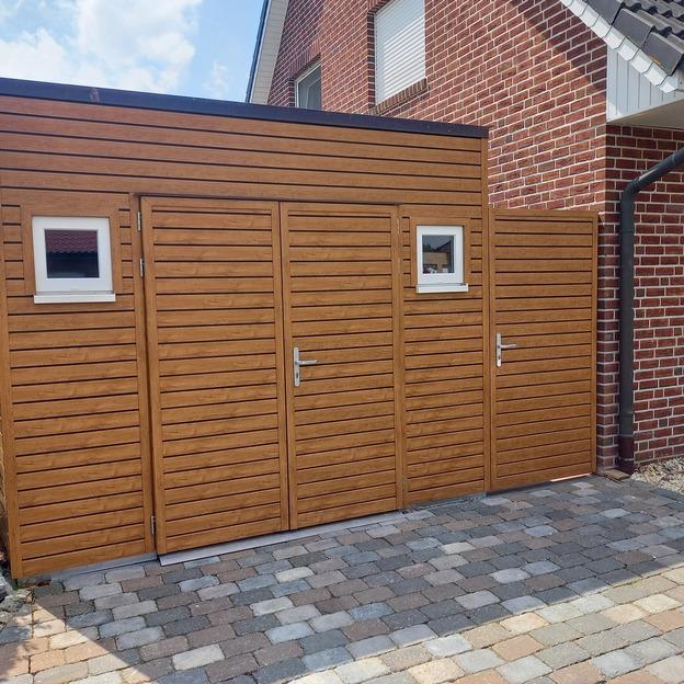 Gartenhaus in moderner Holzoptik mit zwei Türen und kleinen Fenstern, direkt an ein Klinkerhaus angrenzend.