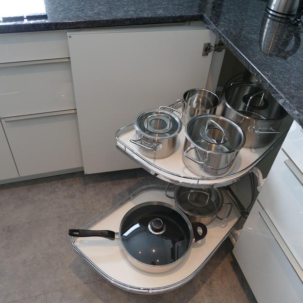 Eine intelligente Stauraumlösung in einer maßgefertigten Küche mit herausziehbarem Topfkarussell unter einer Granitarbeitsplatte.