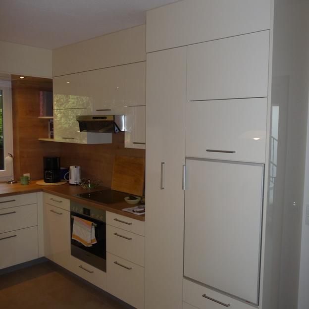 Moderne, weiße Küche nach Maß mit hohen Schränken und eingebauten Geräten, Arbeitsflächen aus Holz und Spiegelrückwand.