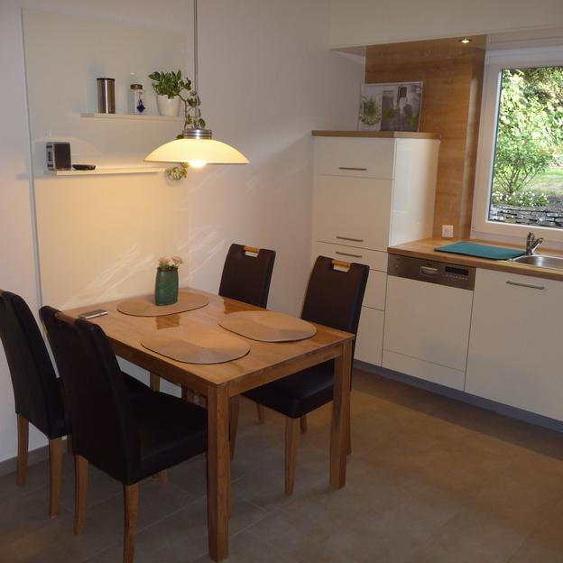 Ein gemütlicher Essbereich mit Holztisch und Stühlen in einer Küche nach Maß, großes Fenster mit Gartenblick.