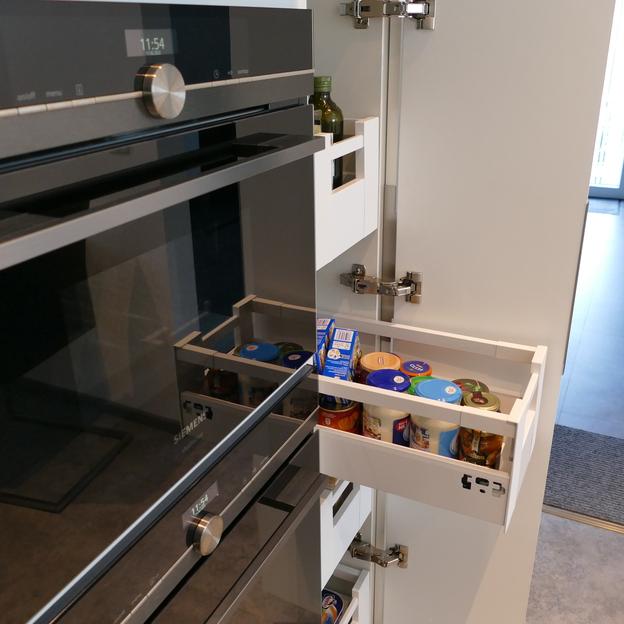 Nahaufnahme von geöffneten Schubladen in einer Küche nach Maß, gefüllt mit Lebensmitteln, neben einem modernen Backofen.