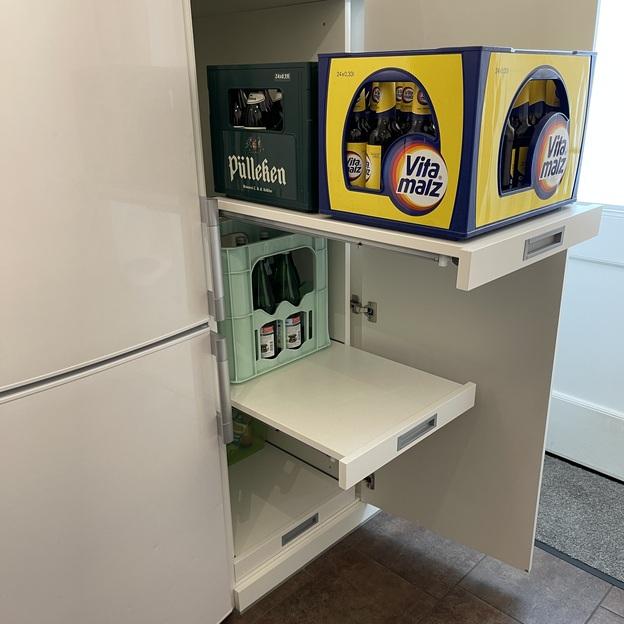 Weißer Wandschrank in einer Küche mit einer geöffneten Tür und herausziehbaren Schubladen