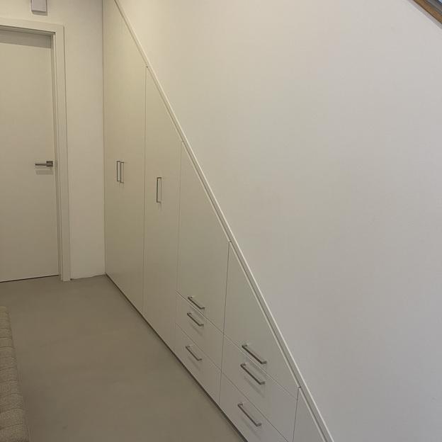 Maßgefertigter Dachschrägenschrank aus weißem Holz unter Treppe