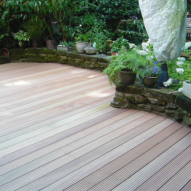 Frisch verlegte Terrassendielen aus Holz, umgeben von niedriger Natursteinmauer mit Blumentöpfen und Gartendekoration.