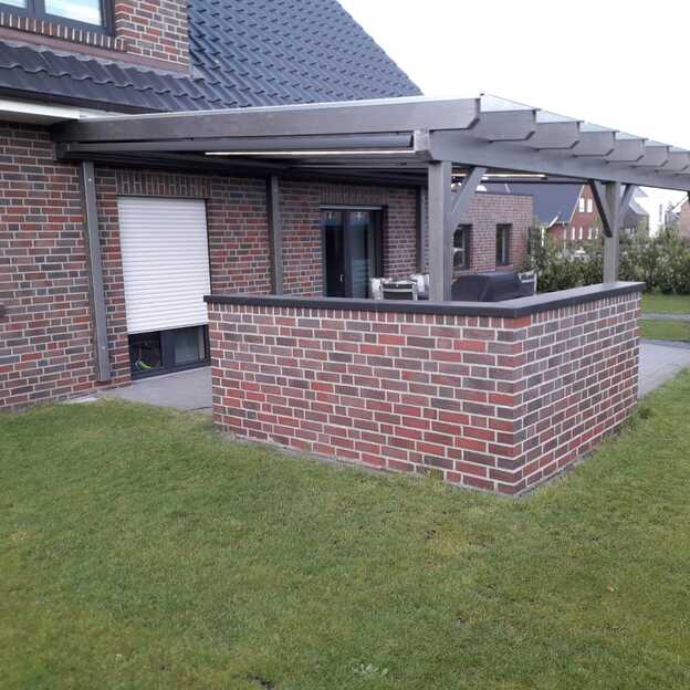errassenüberdachung mit Flachdach an einem Klinkerhaus, ergänzt durch eine gemauerte Einfassung und Gartenlounge.