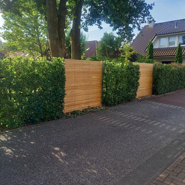 Brauner Holzzaun in einer Auffahrt zwischen einer Hecke