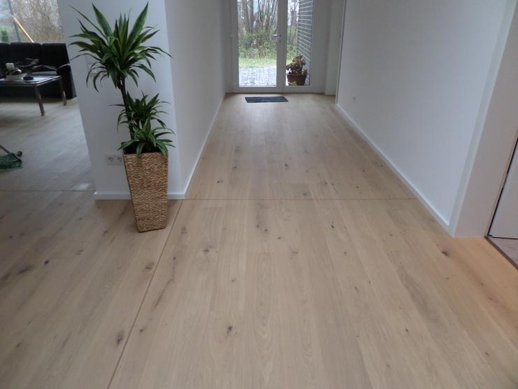 Langer, heller Flur mit breiten Eichenholzdielen, weißen Wänden und einer hohen Zimmerpflanze im geflochtenen Topf.