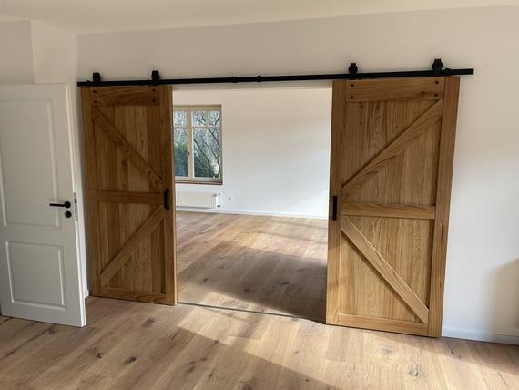 Breite Doppelschiebetür aus massiver Eiche mit schwarzer Laufschiene zwischen zwei hellen Räumen.