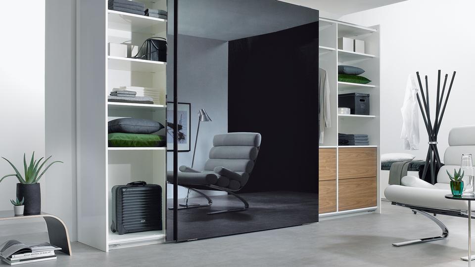 Wohnraumimpression mit abgetrennter dunkler Glasschiebetür für Ruheoase und integrierten Einbauregalen